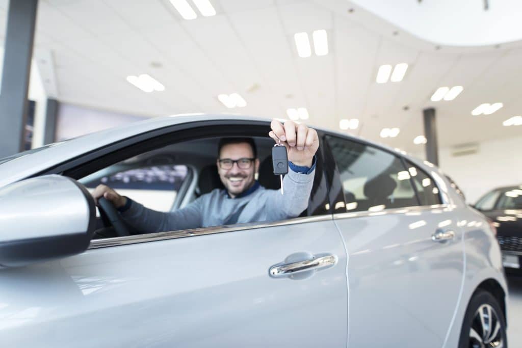 vale-a-pena-comprar-carros-de-leilao-homem-em-carro-com-braco-para-fora-mostrando-a-chave