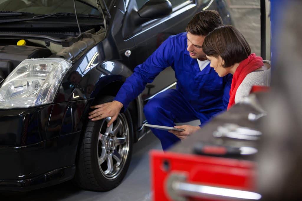 Mecânico mostrando detalhes do pneu de um carro para uma cliente em uma oficina, enquanto ambos discutem sobre a inspeção veicular.