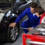 Mecânico mostrando detalhes do pneu de um carro para uma cliente em uma oficina, enquanto ambos discutem sobre a inspeção veicular.