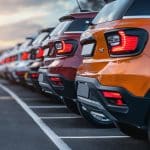 Fila de SUVs estacionados ao ar livre, em um fim de tarde com céu colorido, destacando veículos modernos e prontos para comercialização.