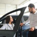 Vendedora apresentando um carro seminovo para uma cliente dentro de uma concessionária iluminada, destacando a interação profissional e o veículo em exibição.
