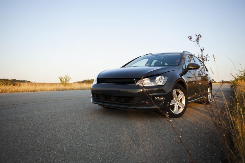 Carro preto estacionado em uma estrada asfaltada ao lado de um campo aberto, sob um céu claro ao entardecer. A cena transmite tranquilidade e liberdade, com a natureza ao fundo em contraste com a modernidade do veículo.