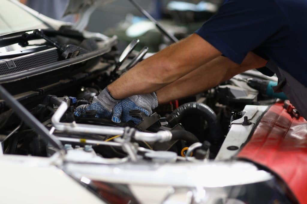 Mecânico realizando reparos no motor de um carro, utilizando luvas de proteção em um ambiente de oficina. A imagem destaca a atenção aos detalhes e a manutenção automotiva profissional.