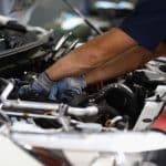 Mecânico realizando reparos no motor de um carro, utilizando luvas de proteção em um ambiente de oficina. A imagem destaca a atenção aos detalhes e a manutenção automotiva profissional.