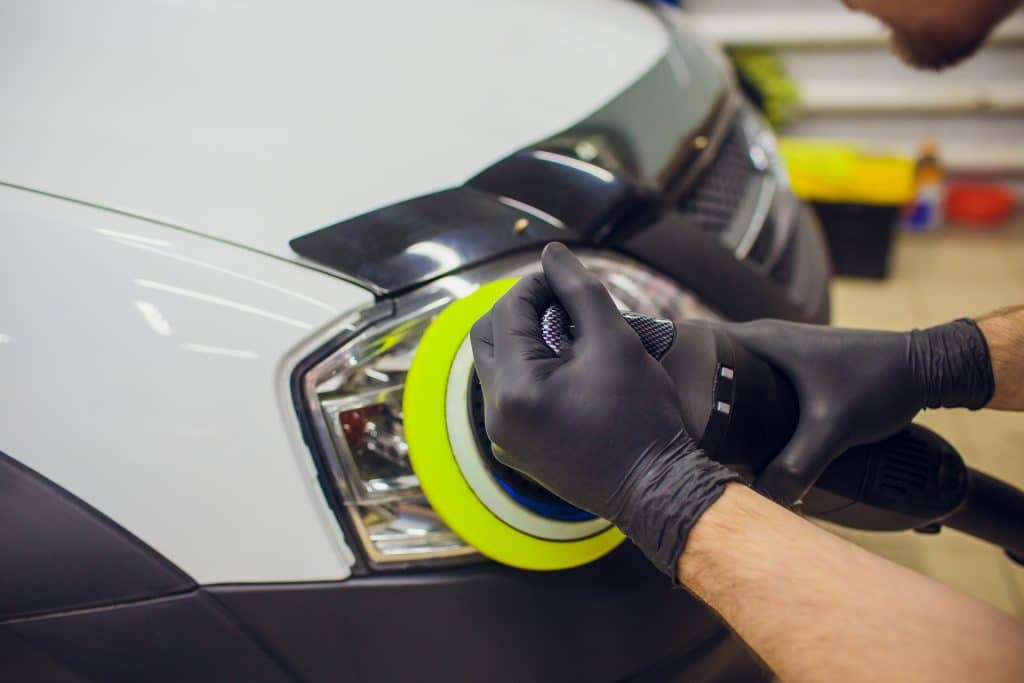 Um mecânico utilizando uma ferramenta elétrica para polir e restaurar o brilho do farol de um carro em uma oficina automotiva.