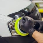 Um mecânico utilizando uma ferramenta elétrica para polir e restaurar o brilho do farol de um carro em uma oficina automotiva.