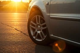 Imagem de um carro estacionado ao pôr do sol, com foco na roda dianteira e a estrada ao fundo.