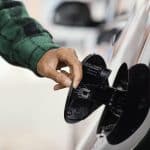 Pessoa abrindo a tampa do tanque de combustível de um carro para abastecer.